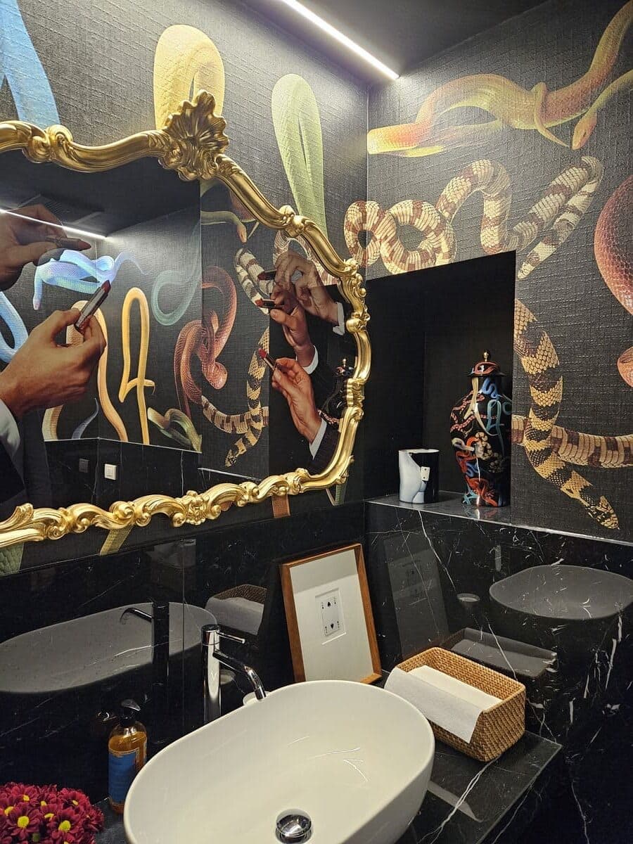 Bagno con specchio barocco dorato, wallpaper Toiletpaper e lavabo su piano scuro