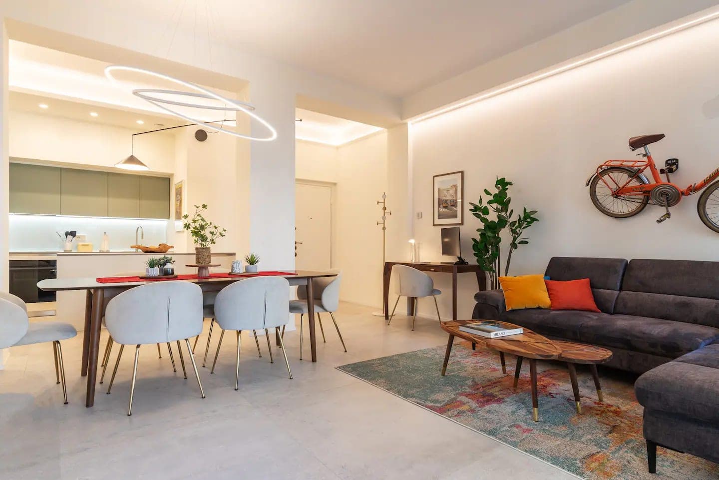 Vista panoramica dell open space con cucina verde salvia, tavolo da pranzo, zona living e porta ingresso