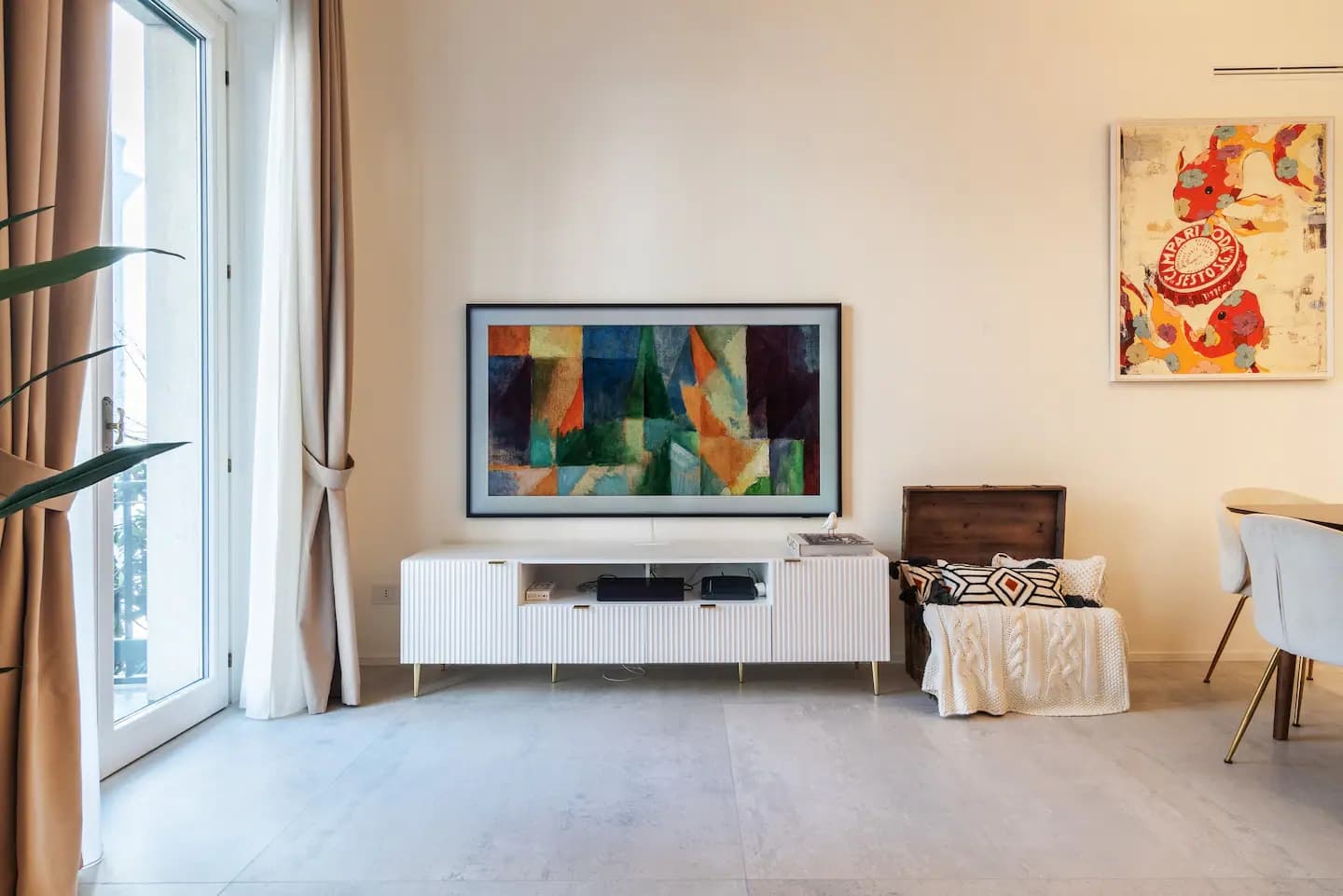 Parete TV con Samsung Frame, consolle bianca, baule vintage e dipinto astratto accanto alla portafinestra