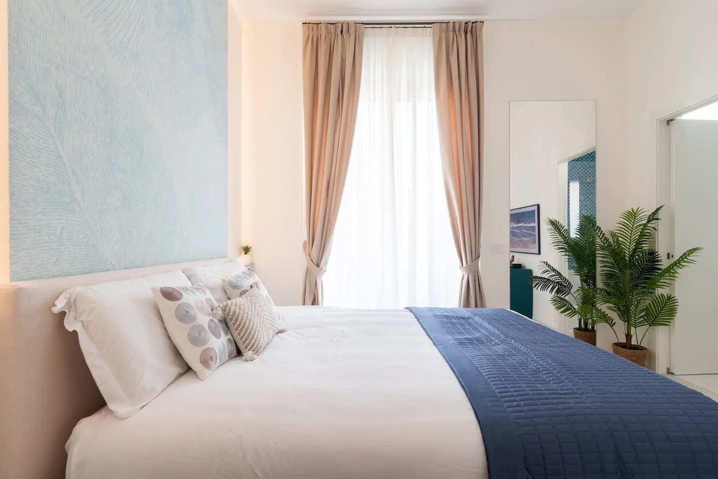 Camera principale con letto, carta da parati botanica azzurra, tende beige e palma decorativa
