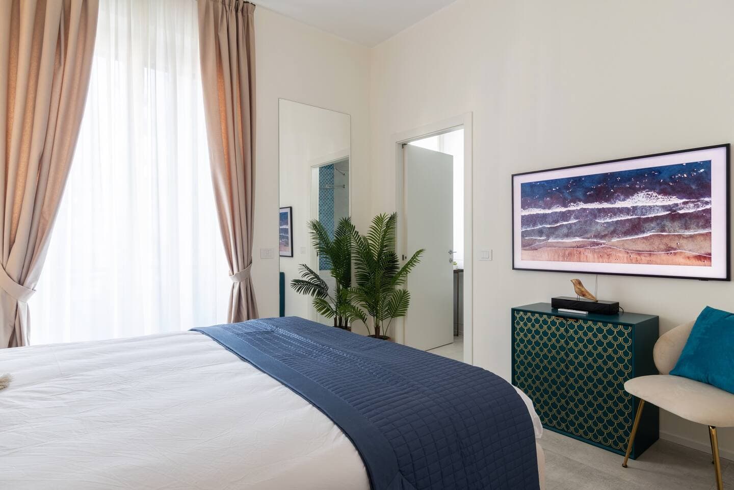 Camera principale con finestra, palma, cassettiera decorata e stampa marina a parete