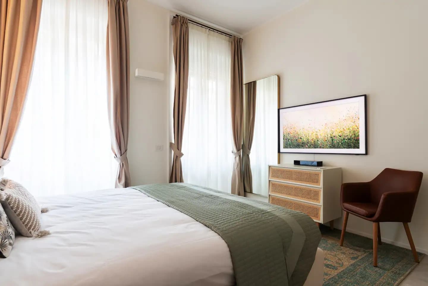 Seconda camera con letto e plaid verde, due finestre, cassettiera in rattan con Samsung Frame TV e poltrona in pelle