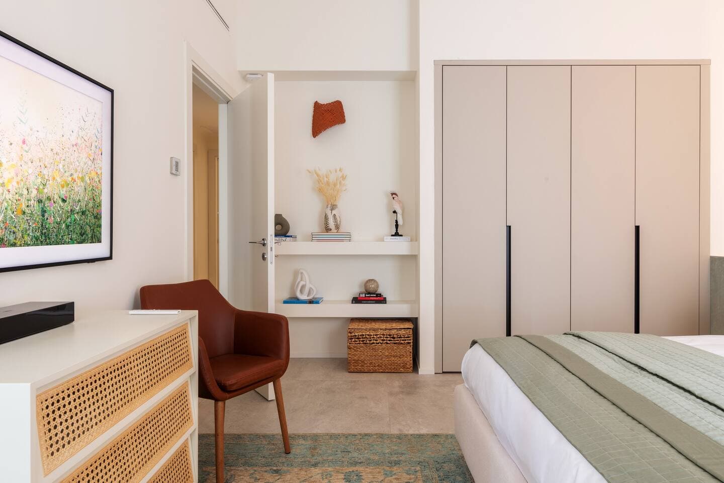 Seconda camera con cassettiera rattan, Samsung Frame TV, poltrona cognac e nicchia con libri decorativi
