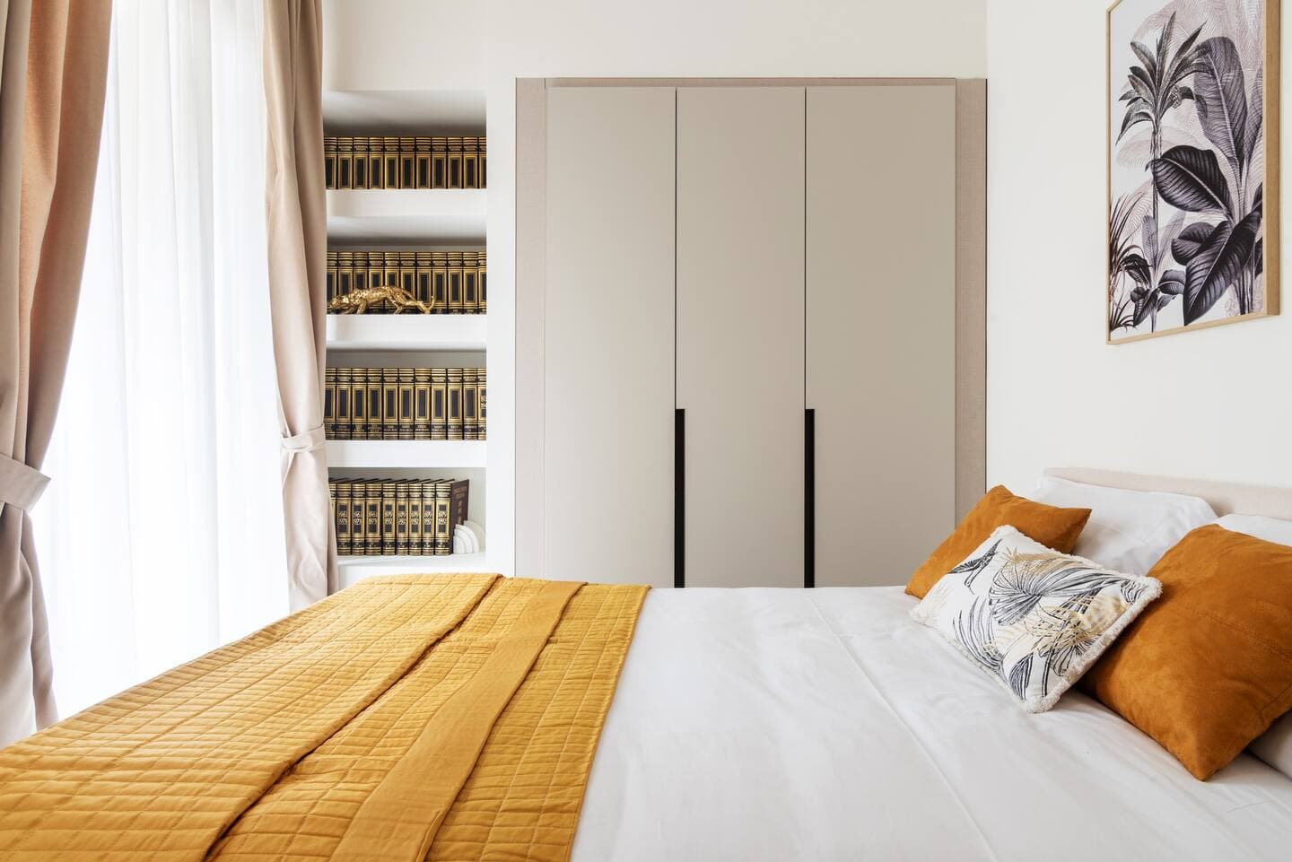 Terza camera con letto senape, libreria con volumi dorati, armadio e stampa botanica a parete