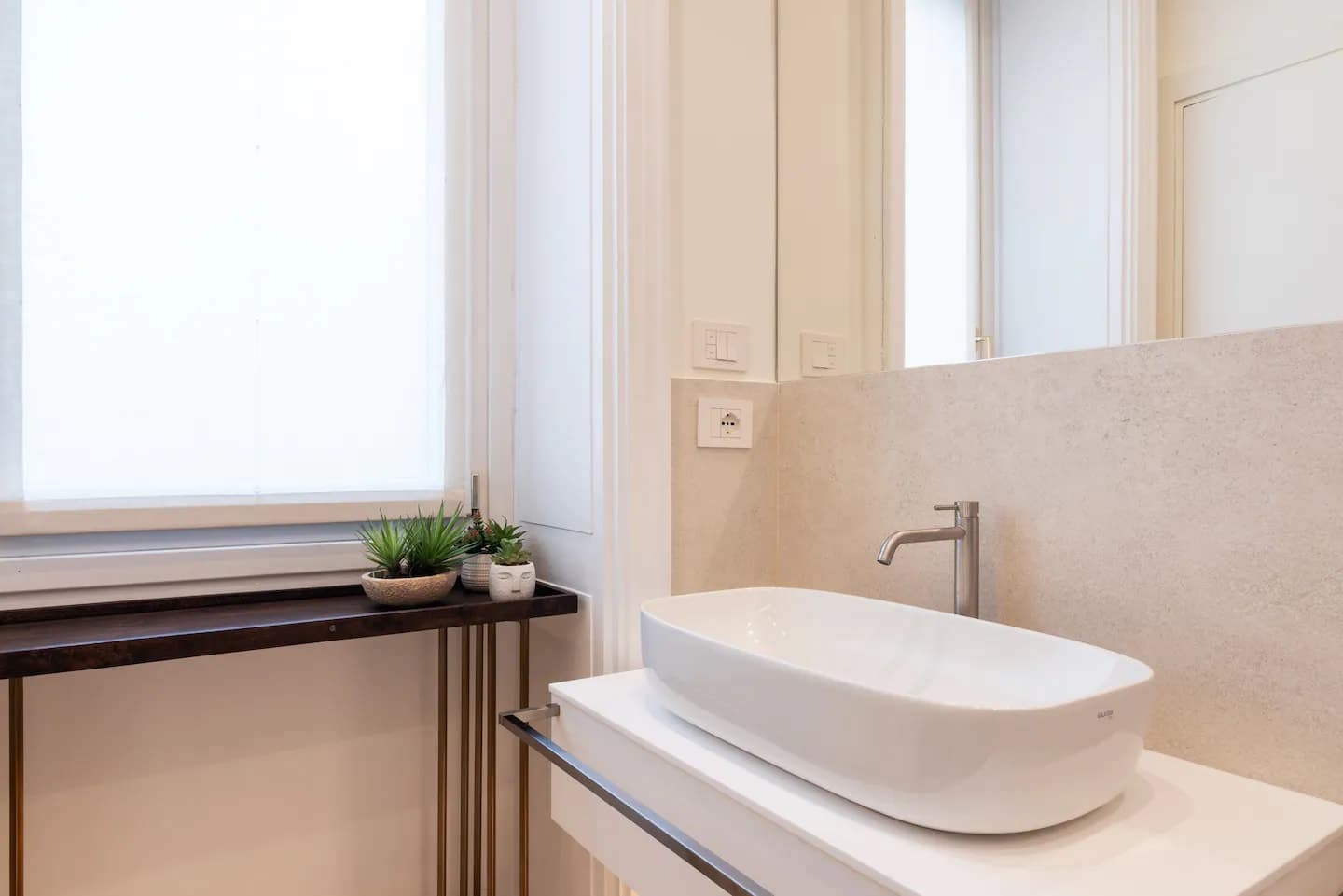 Lavabo bagno con catino bianco su mobile sospeso, rubinetteria alta e rivestimento effetto pietra beige