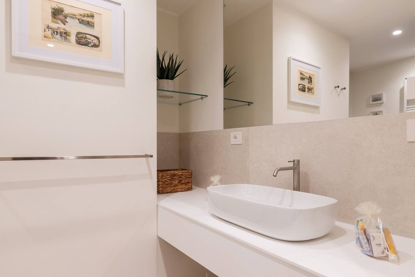 Dettaglio lavabo secondo bagno con catino bianco, mosaico beige, specchio e kit di benvenuto