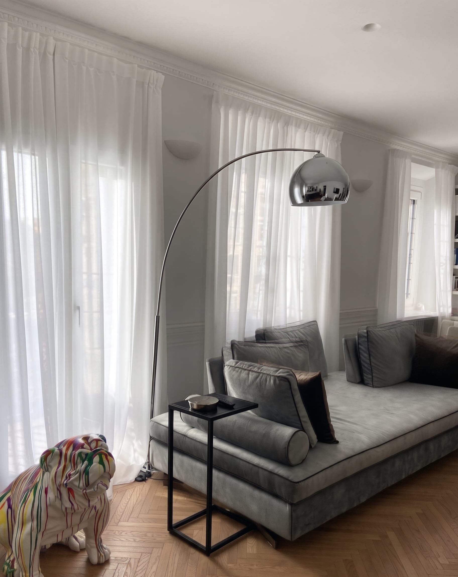 Soggiorno con divano grigio, lampada ad arco cromata e scultura bulldog colorata