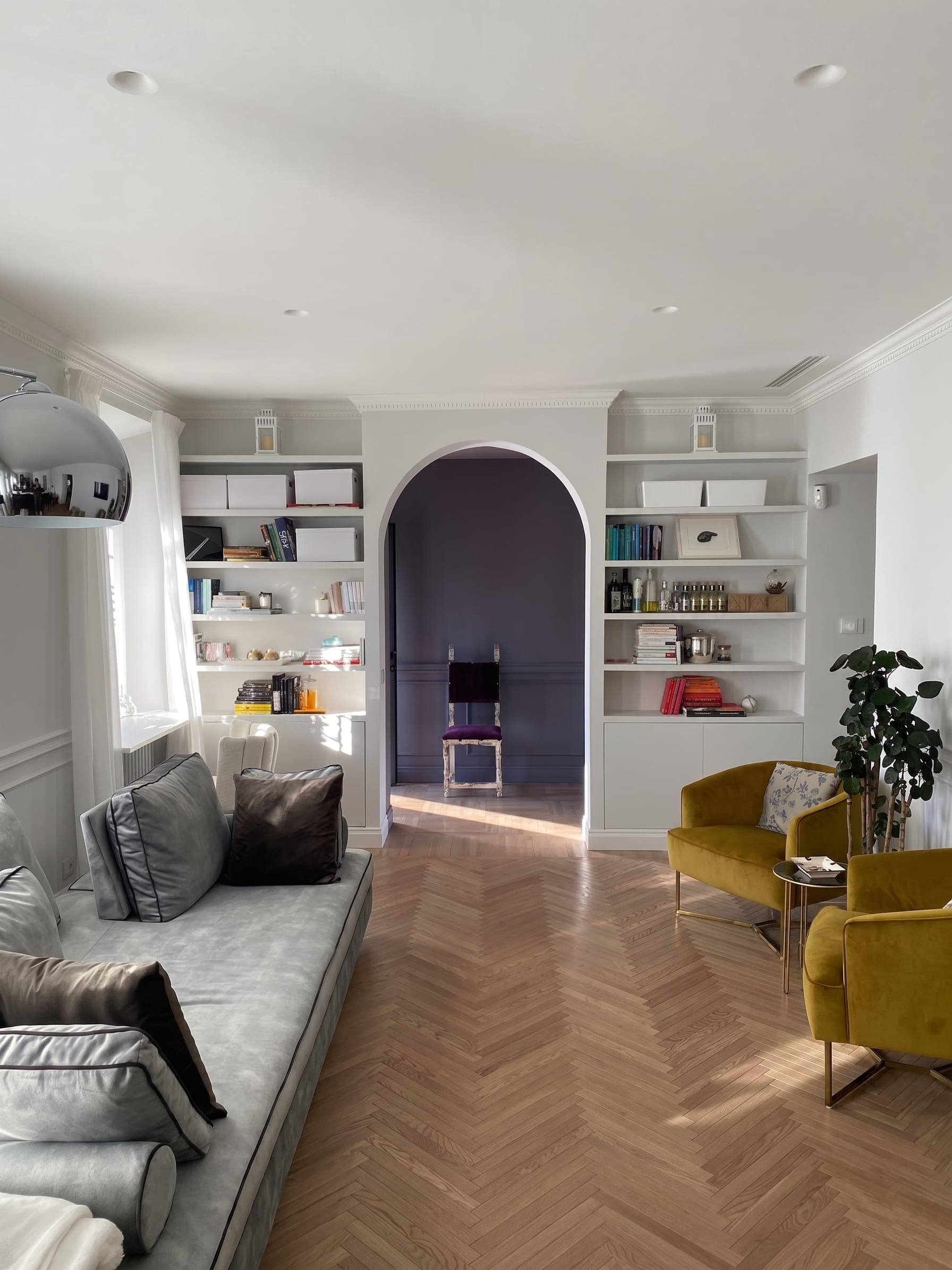 Salone con libreria su misura, arco viola, poltrona senape e parquet a spina