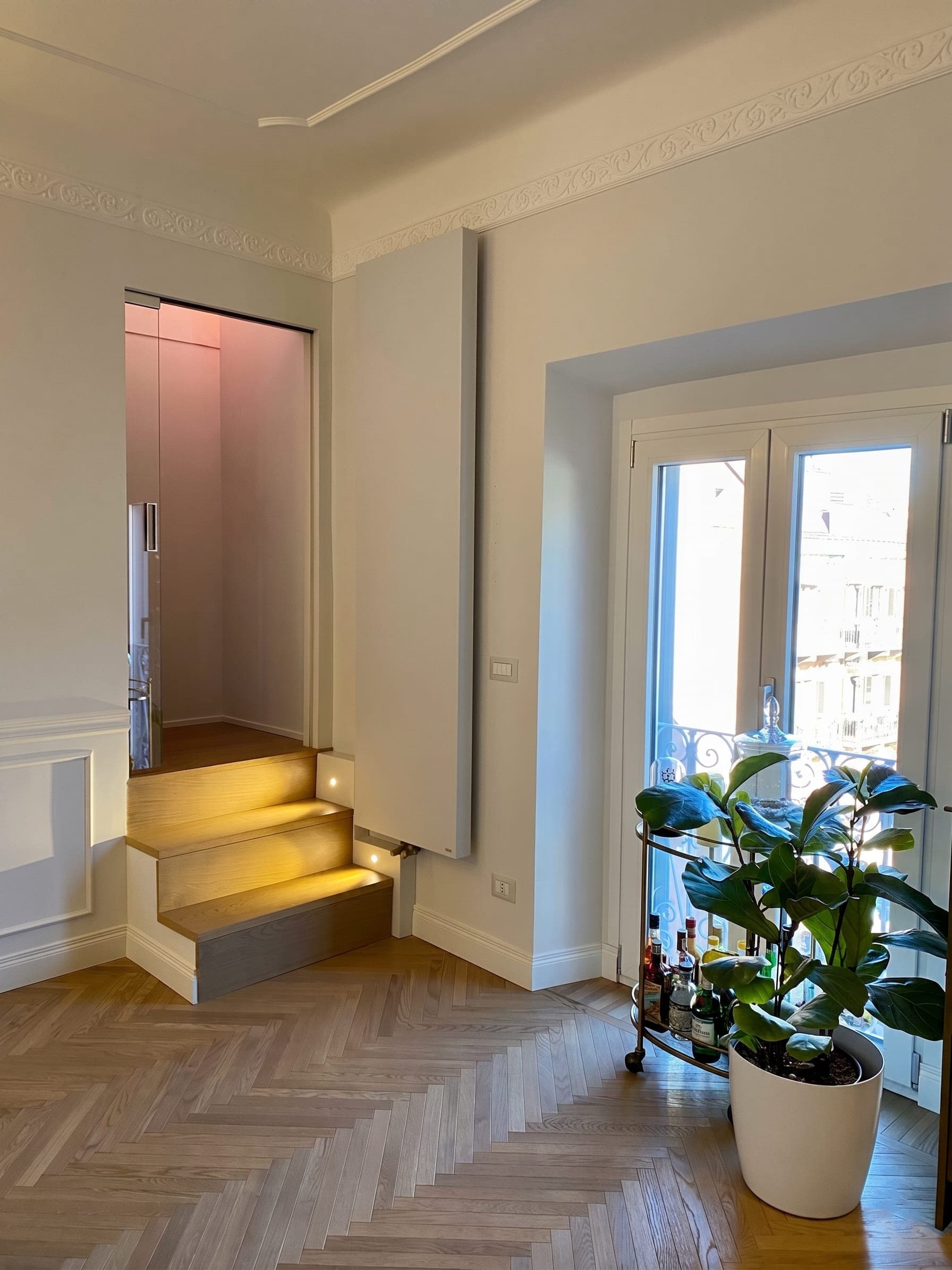 Scala interna illuminata con gradini in legno chiaro e cornici decorative a parete