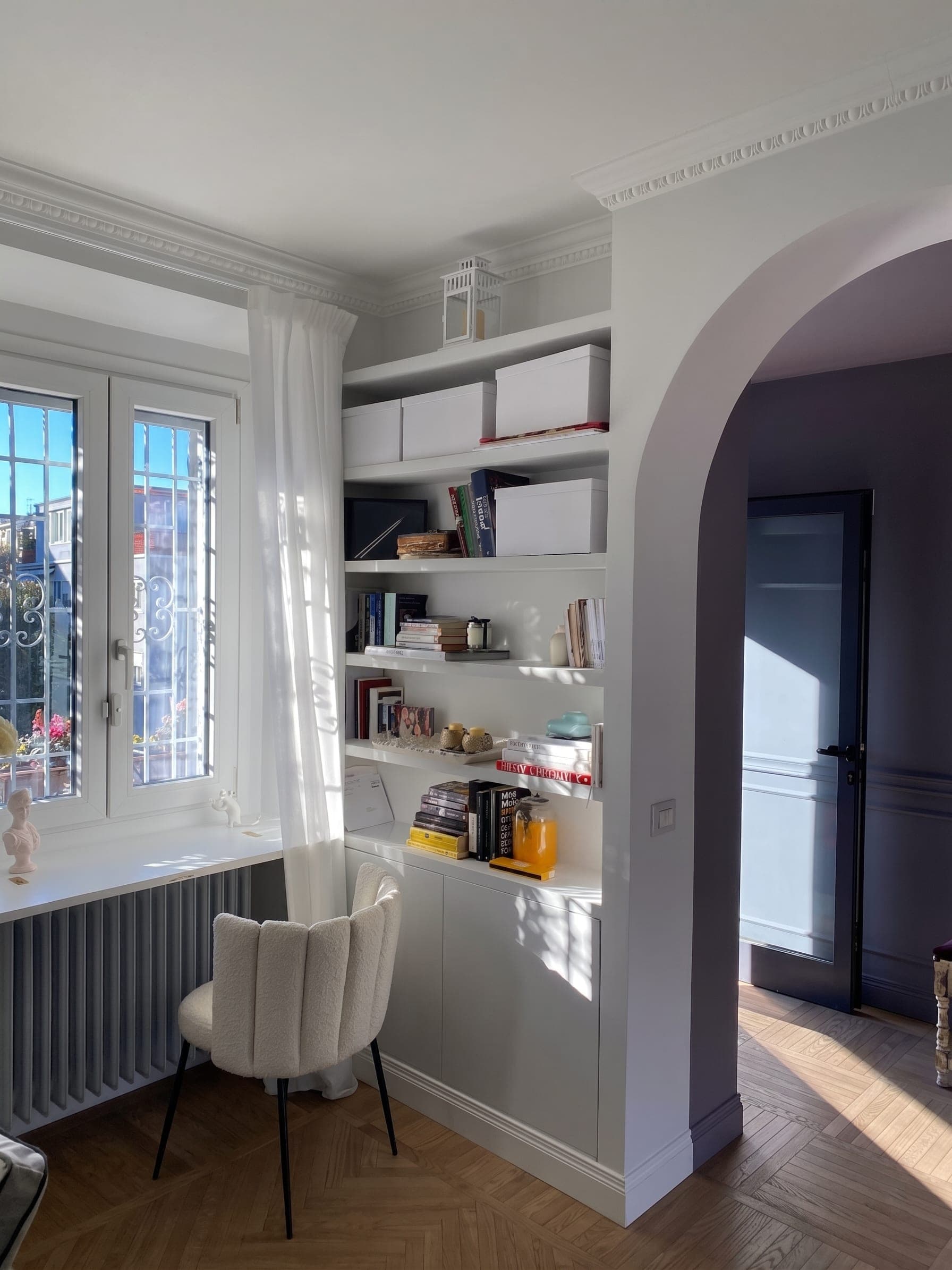 Angolo studio con libreria bianca, poltroncina bouclé e finestra con luce naturale