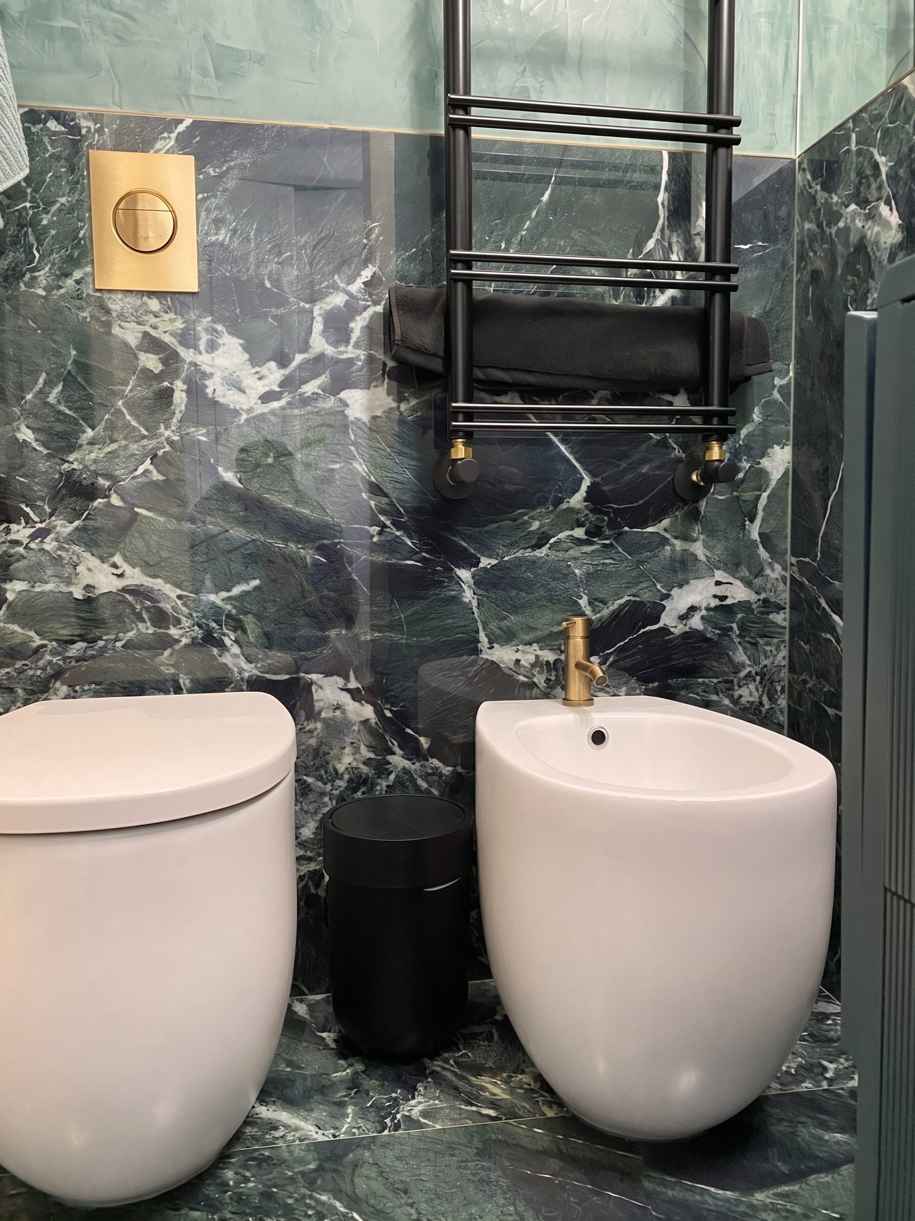 Bagno con rivestimento in marmo verde scuro, sanitari sospesi e rubinetteria dorata