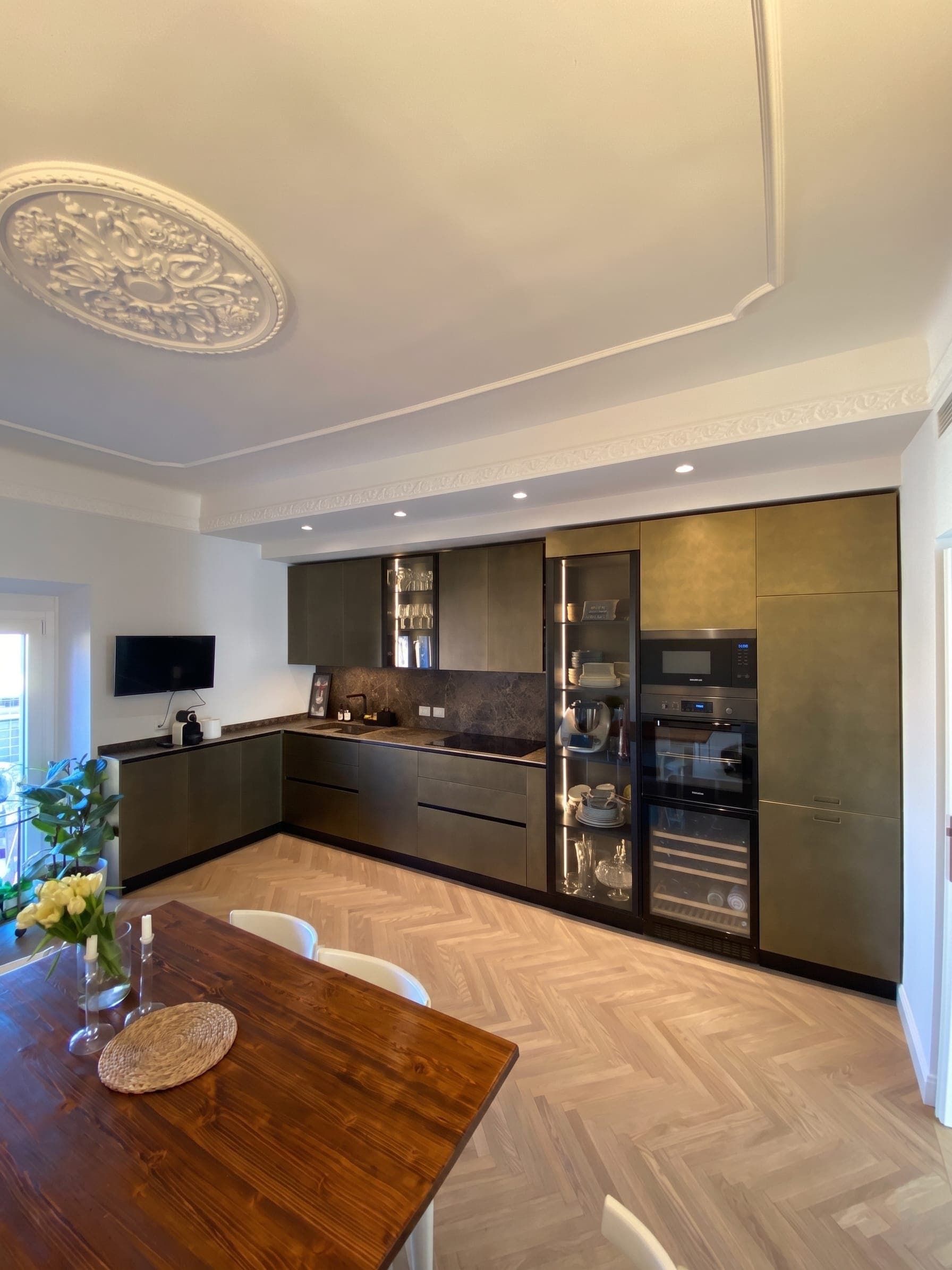 Cucina a L con ante scure, elettrodomestici integrati, rosone decorativo e parquet a spina