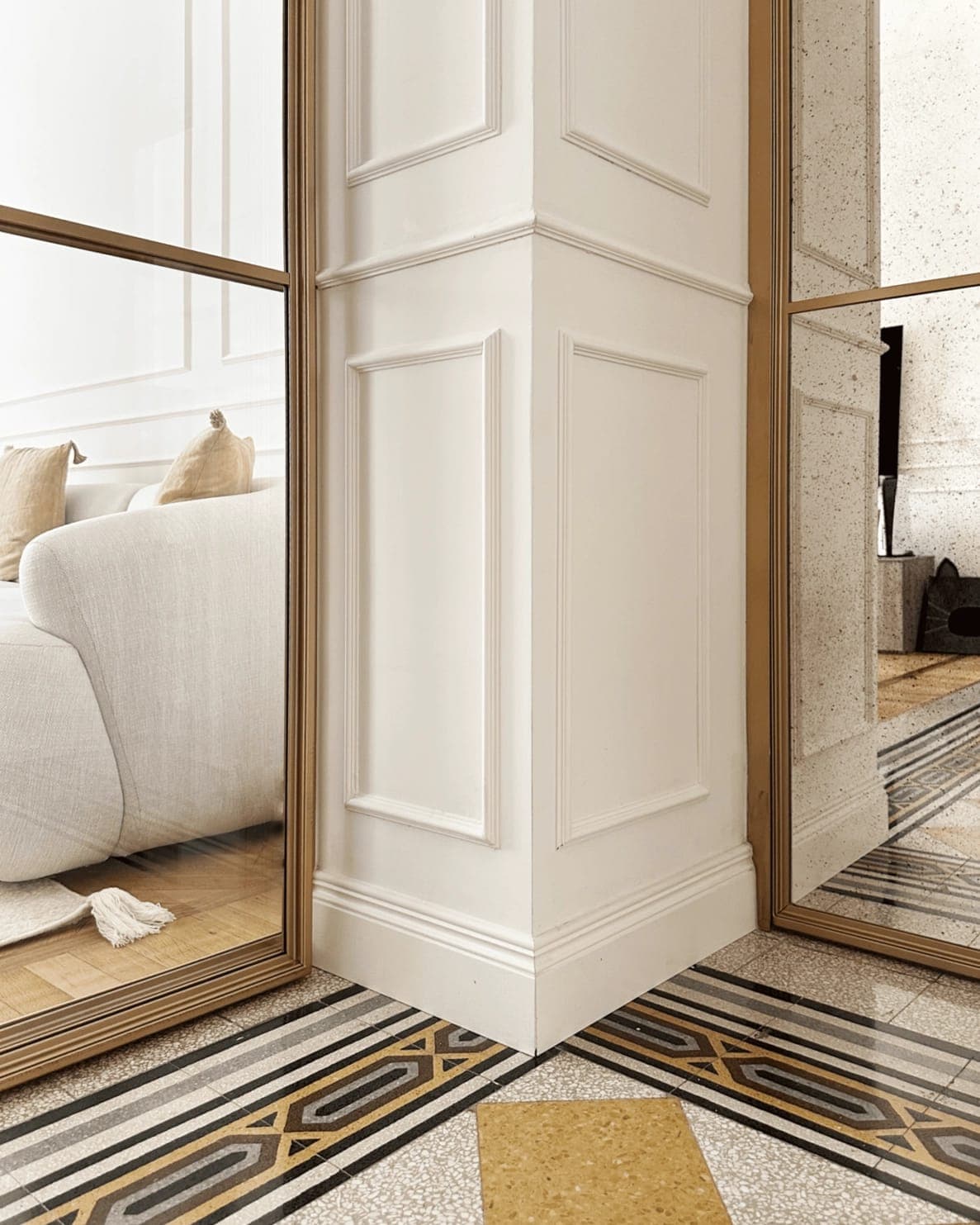 Dettaglio divano e boiserie bianca con scorcio verso stanza con pavimento storico decorato