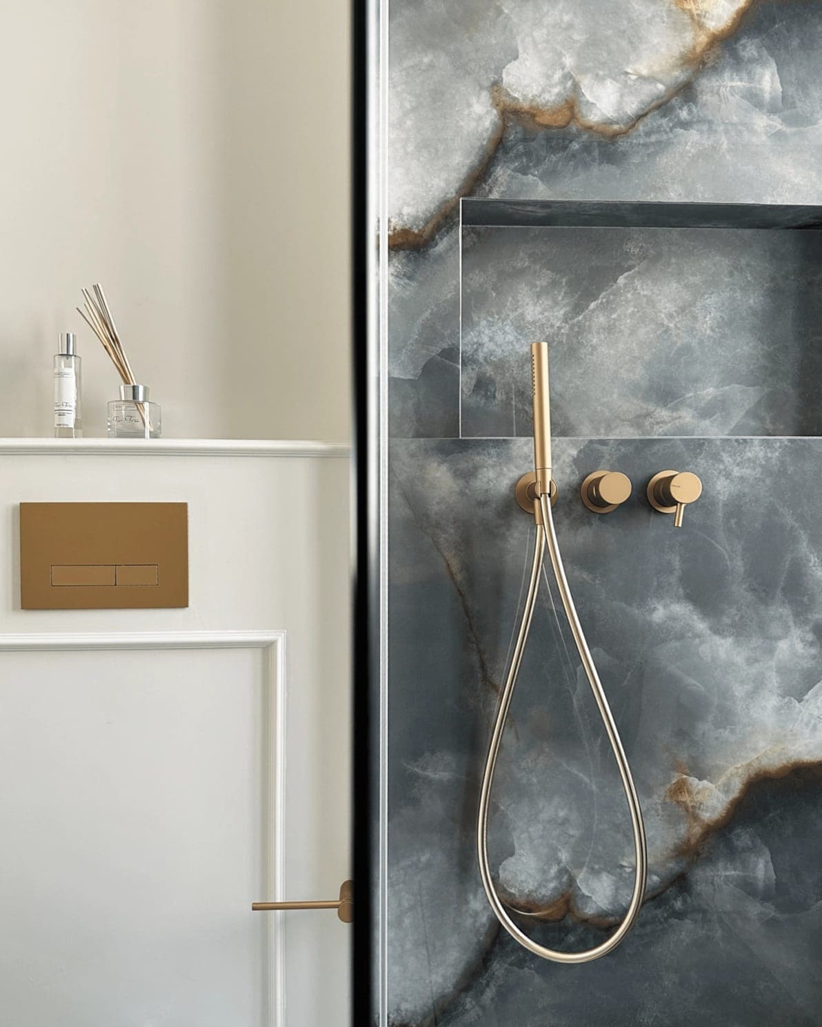 Dettaglio bagno con placca di scarico in ottone, parete scura e doccetta in ottone