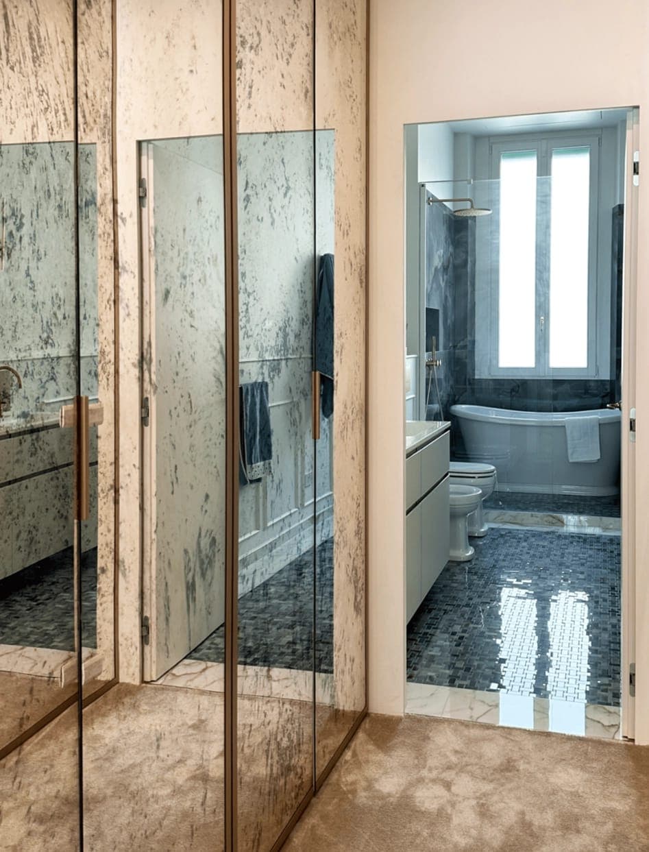 Bagno con specchio anticato a tutta parete, pavimento scuro e vasca da bagno