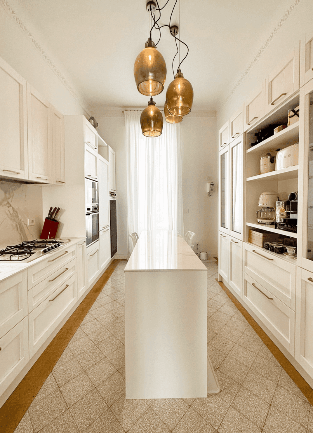 Cucina con ante a cornice bianche, piano cottura a gas e lampade a sospensione in ottone