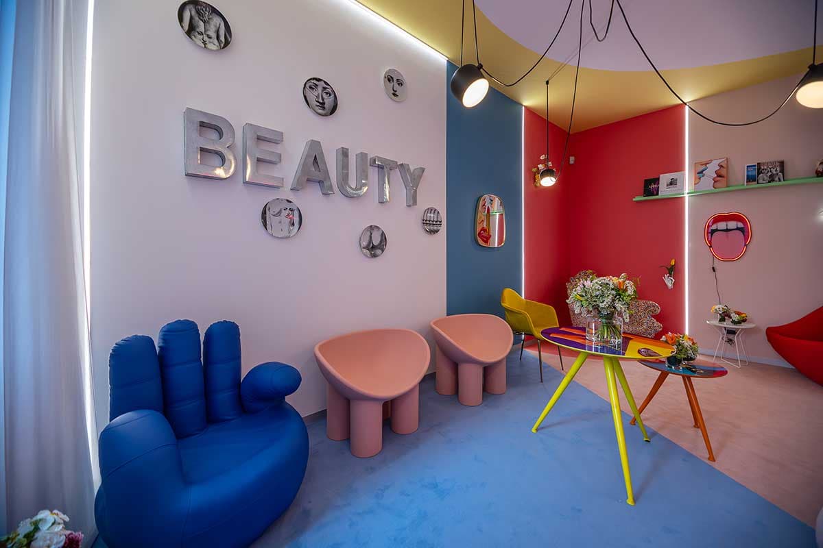 Sala attesa con poltrona blu a forma di mano, sedute rosa e scritta BEAUTY a parete