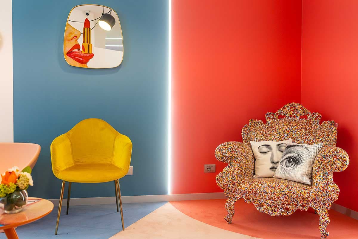 Poltrona gialla, specchio pop art e poltrona barocca con cuscino Fornasetti su parete rossa