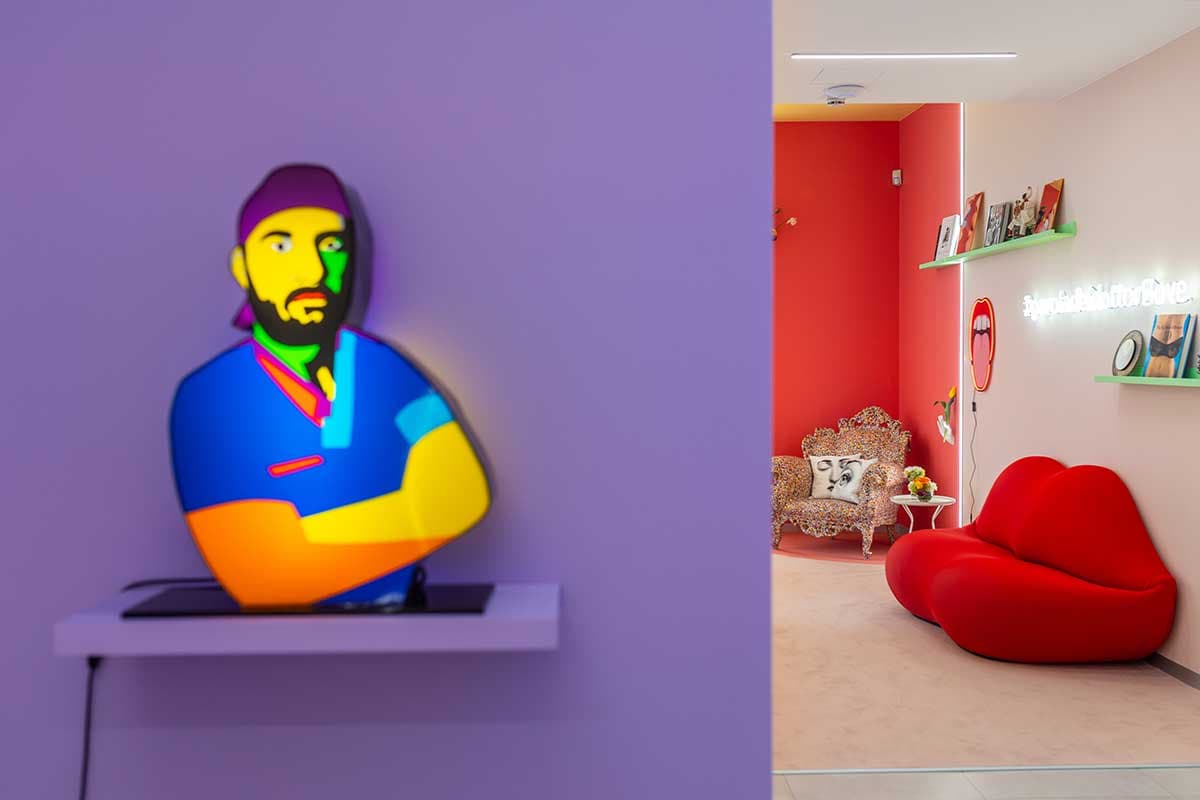 Opera pop art illuminata su parete viola e vista sala con divano labbra rosso e poltrona barocca
