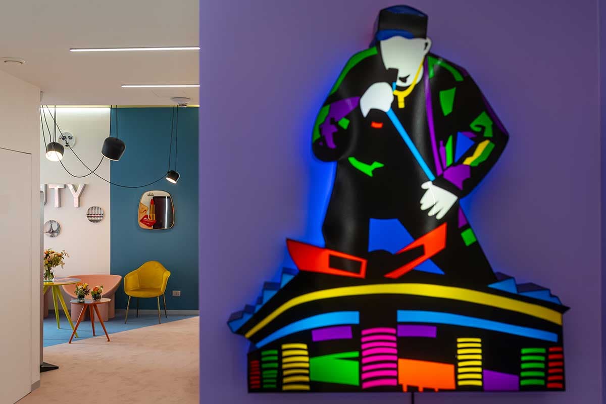 Corridoio con lampade sospese, parete blu e opera neon pop art su sfondo viola