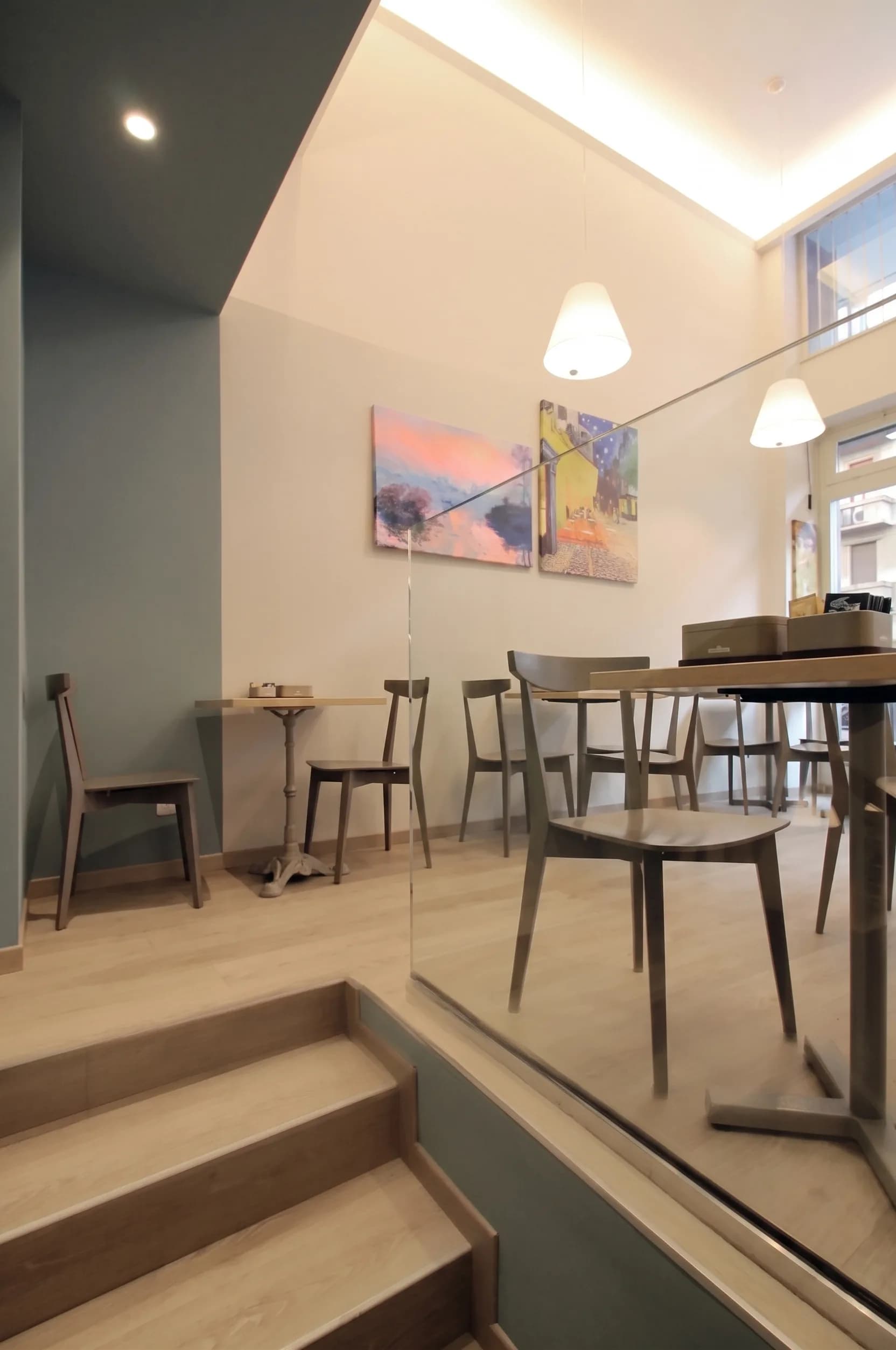 Piano superiore con gradini in legno, parete salvia, tavoli e quadro colorato a parete