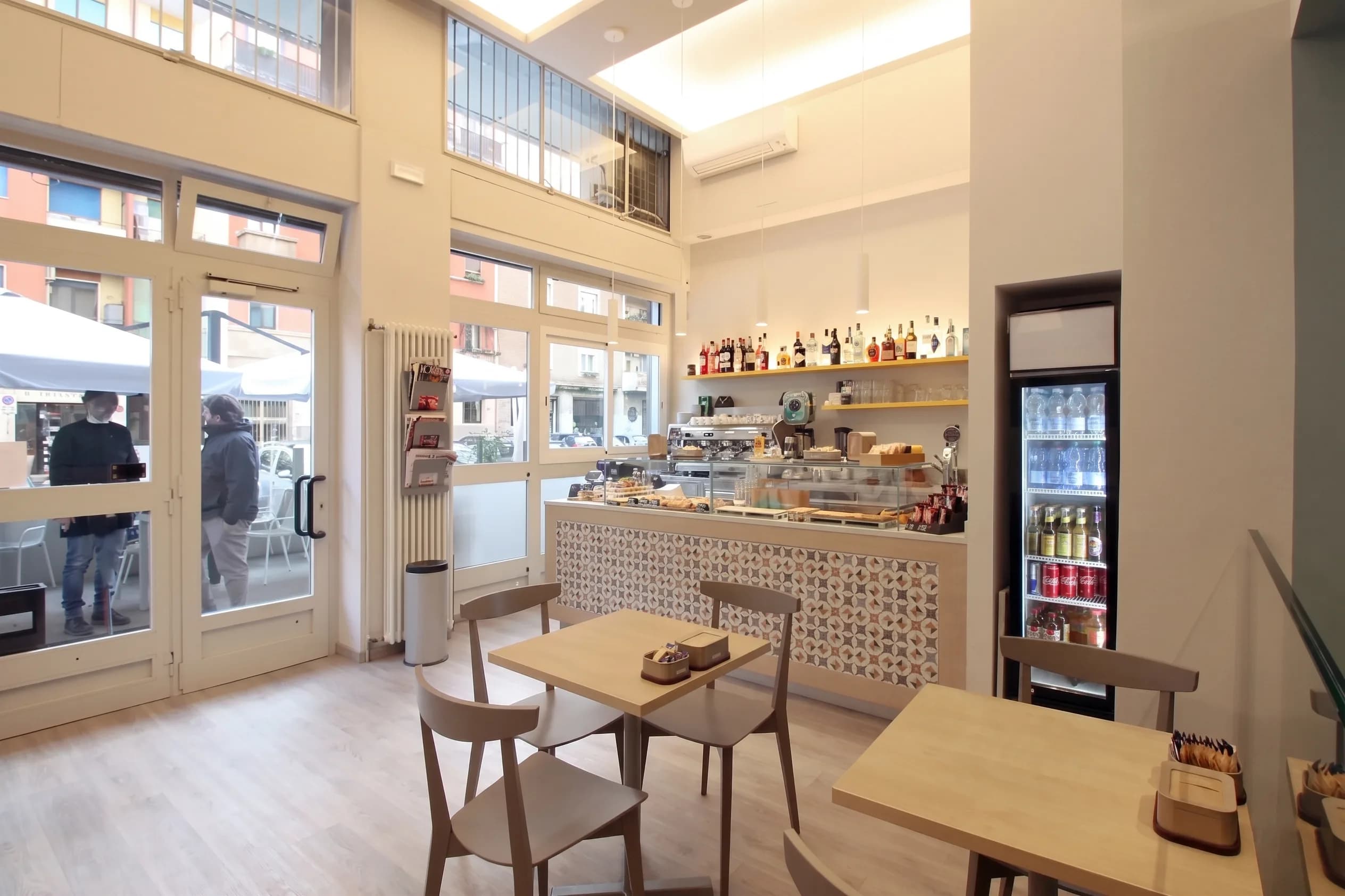 Sala bar con bancone decorato a piastrelle, vetrina dolci, vetrate alte e luce naturale