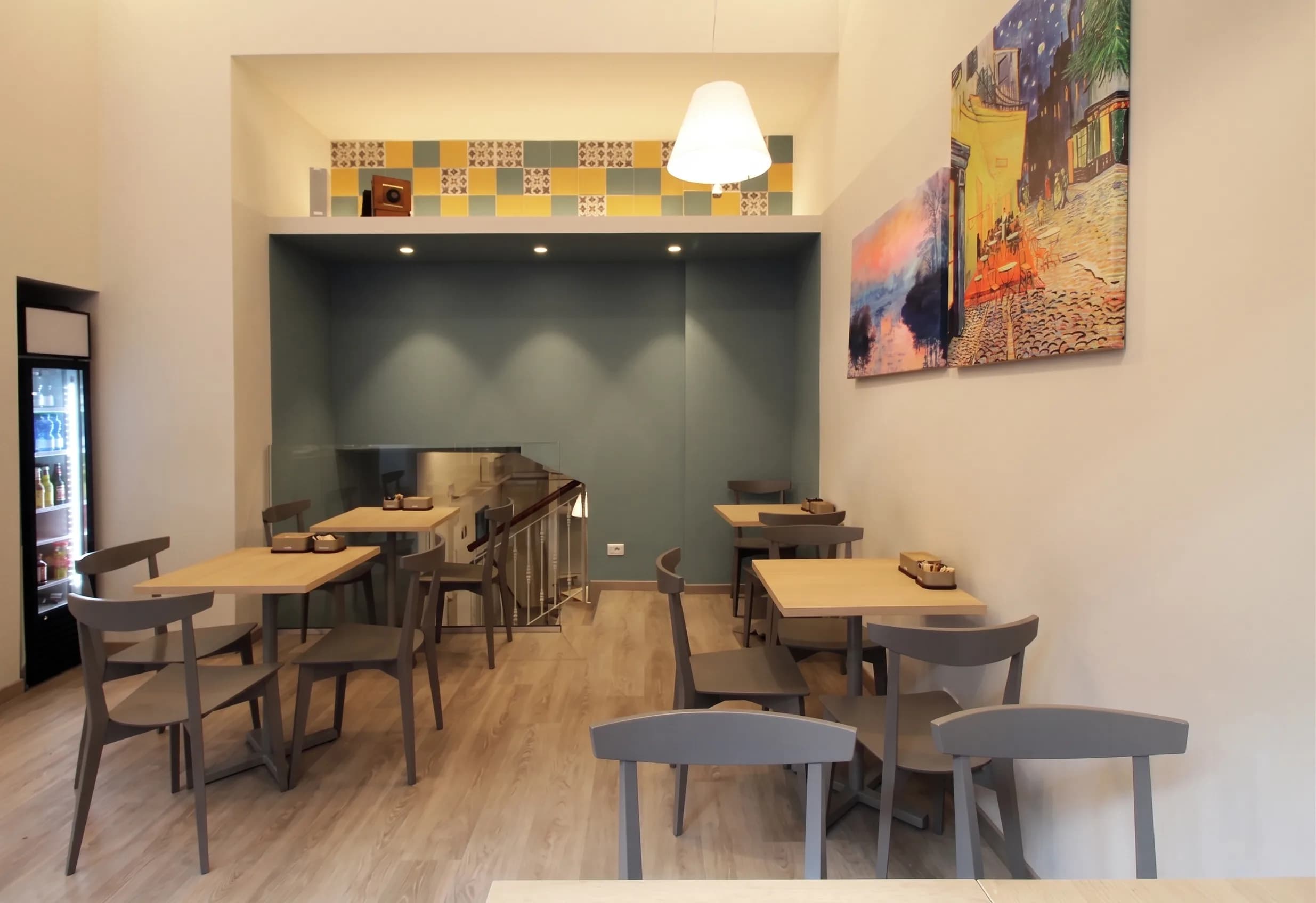 Sala con tavoli, nicchia verde salvia con piastrelle colorate e quadro impressionista a parete