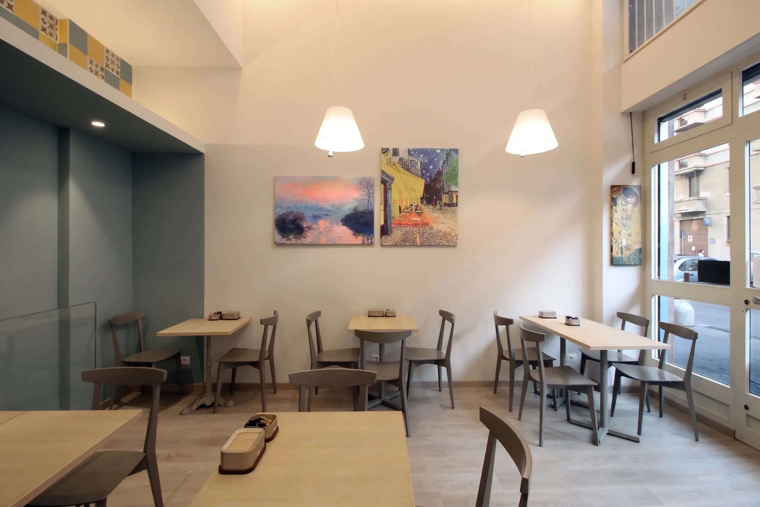 Sala con tavoli, quadri impressionisti, piastrelle decorative al soppalco e vetrate su strada