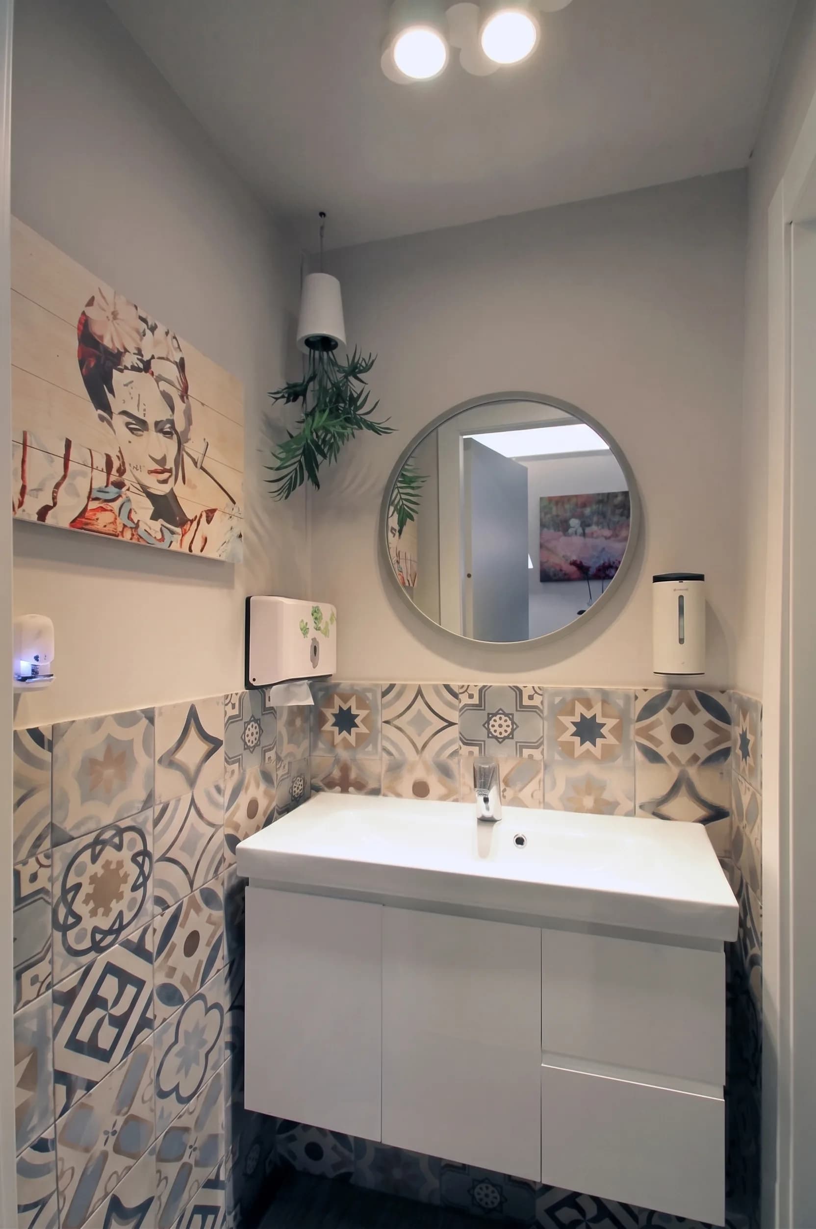 Bagno con piastrelle cementine decorative, lavabo sospeso, specchio tondo e arte a parete