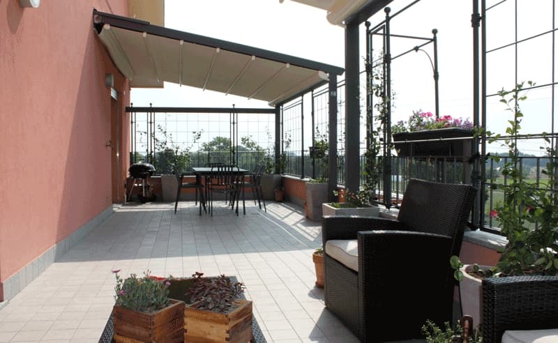 Terrazza con tenda da sole, poltrone in rattan, tavolo da pranzo e fioriere