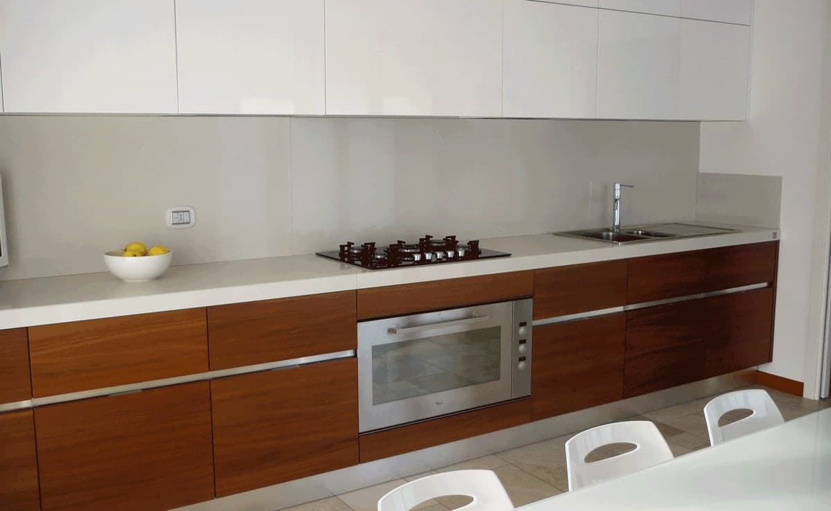 Cucina lineare con basi in legno, pensili bianchi, forno incassato e piano cottura a gas