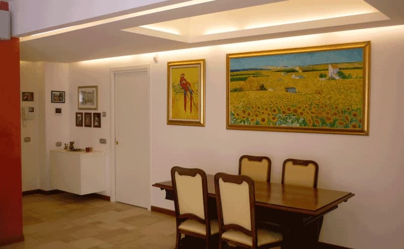 Sala da pranzo con tavolo classico, quadri paesaggistici con girasoli e controsoffitto LED