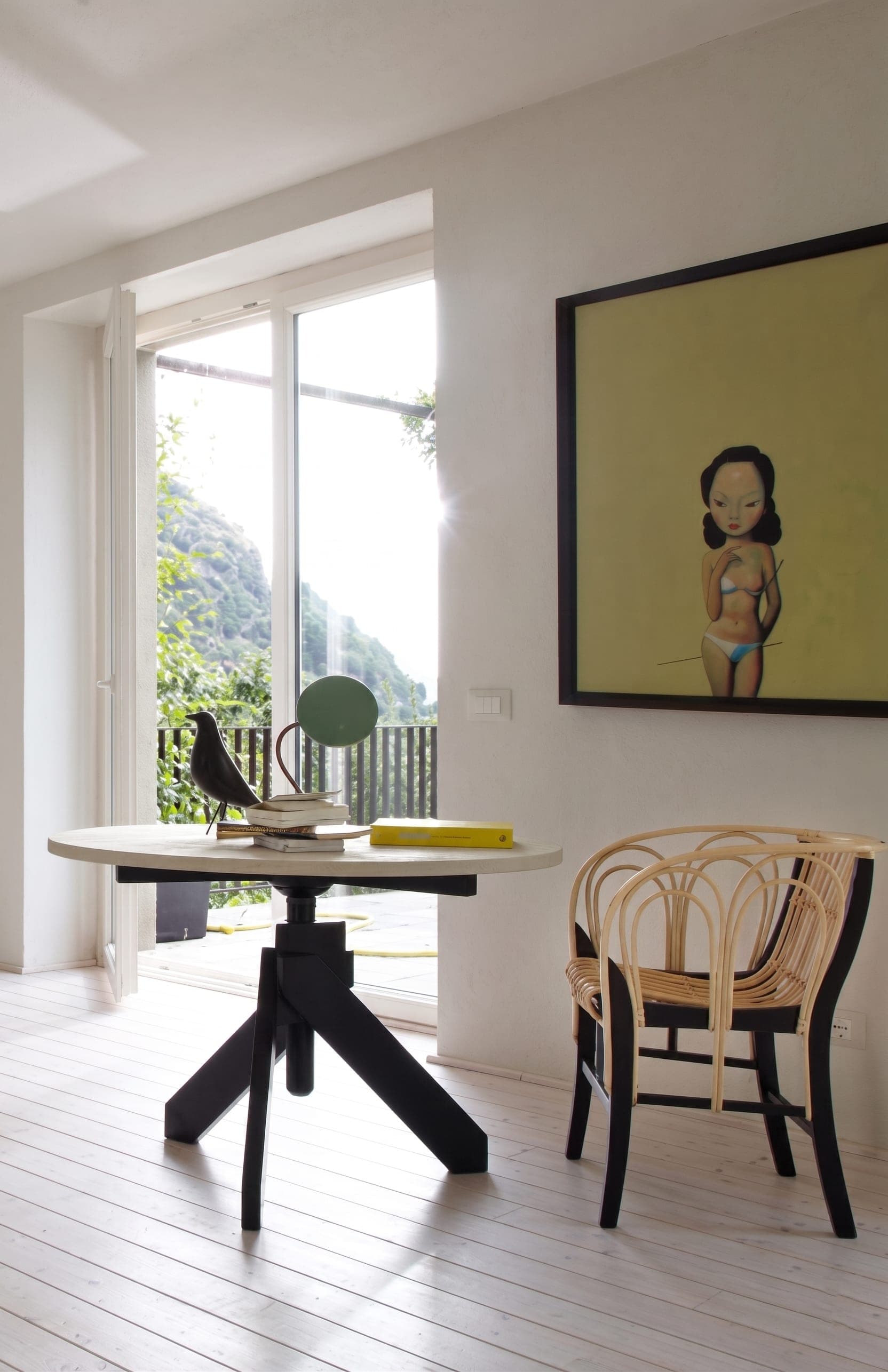Zona pranzo con tavolo design e quadro, amaca gialla con vista lago dalle finestre