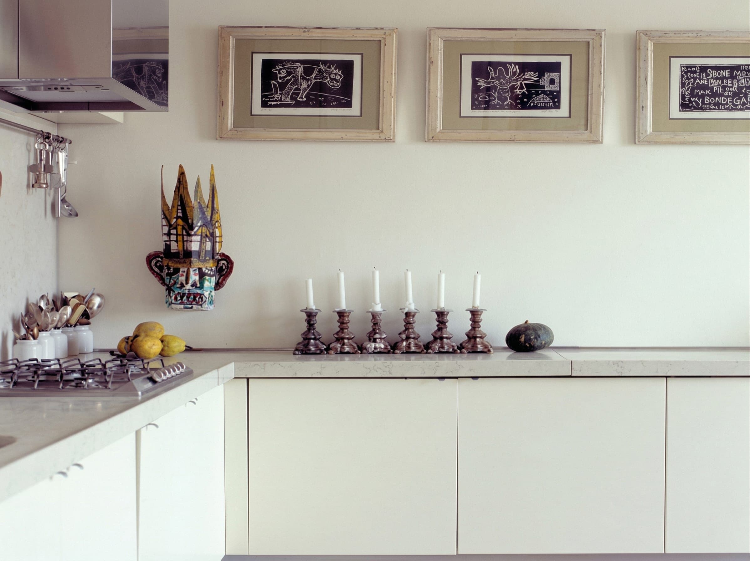 Cucina bianca con candelabri, maschera decorativa, quadri incorniciati e piano cottura