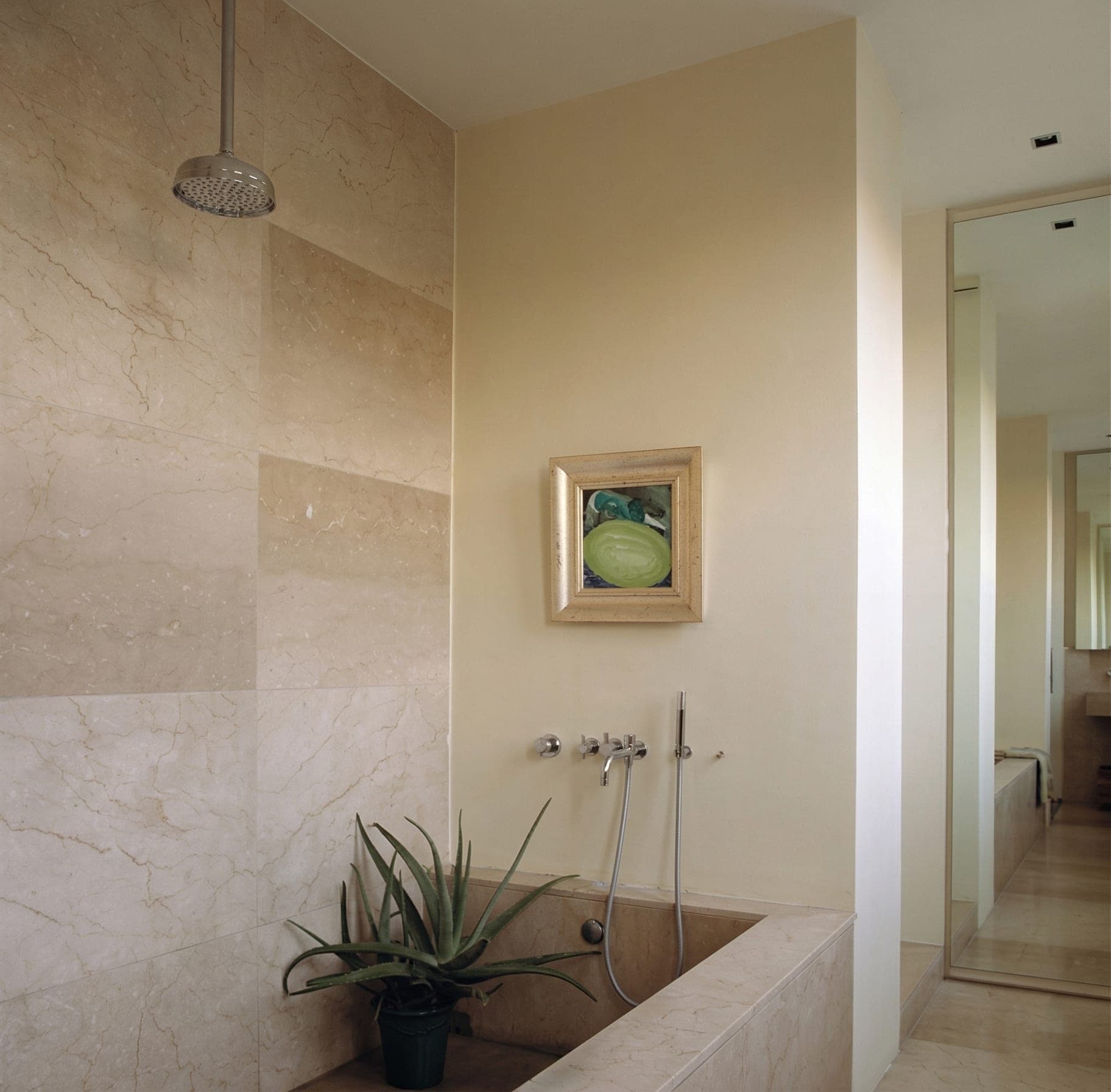 Bagno con vasca incassata, rivestimento chiaro, soffione a pioggia e pianta