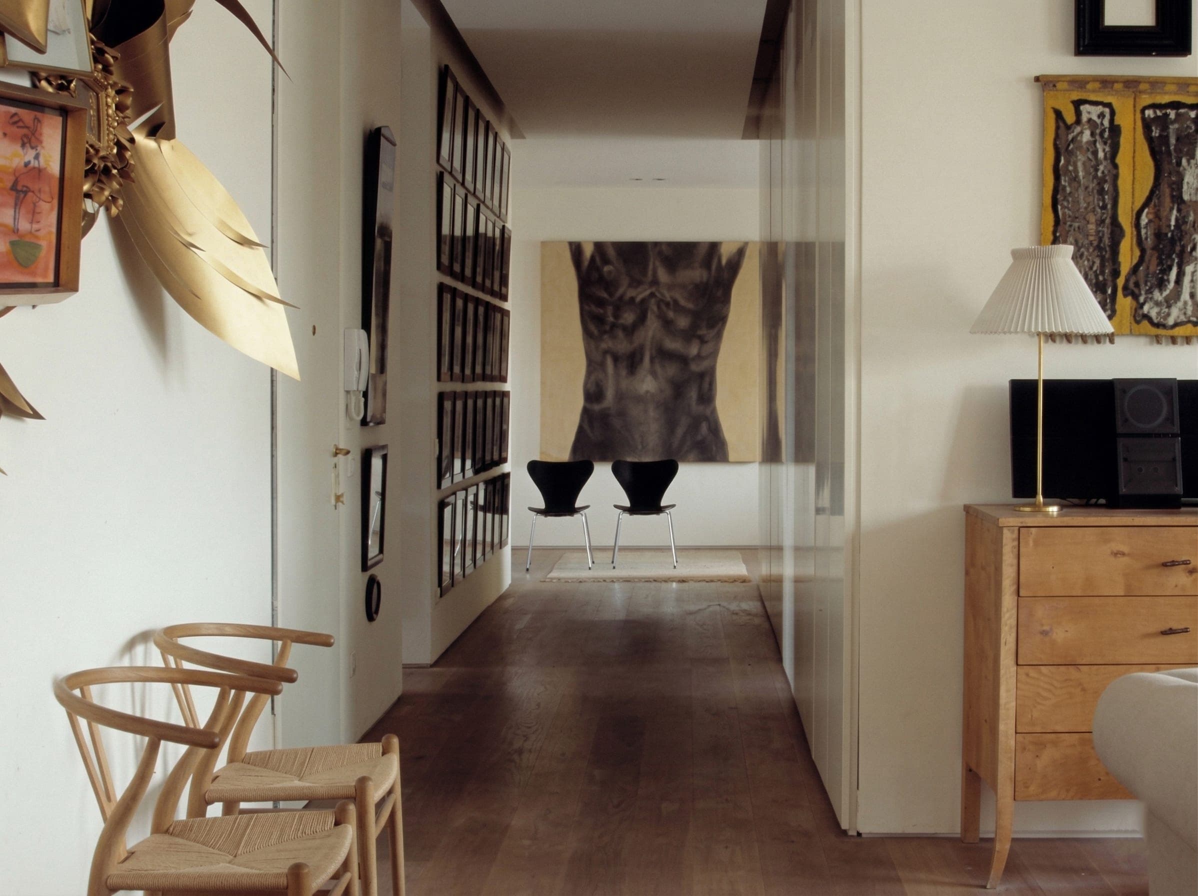 Sala con sedie Wishbone, scultura dorata sospesa, quadri e cassettiera vintage